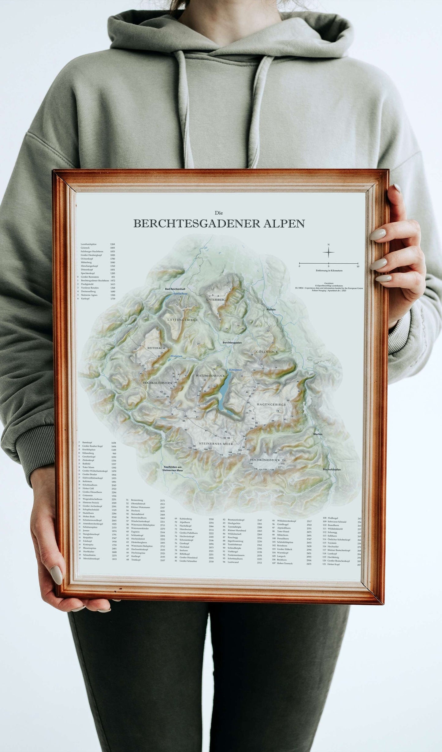 Eine Frau hält eine gerahmte Karte Berchtesgadener Alpen vor ihrem Körper