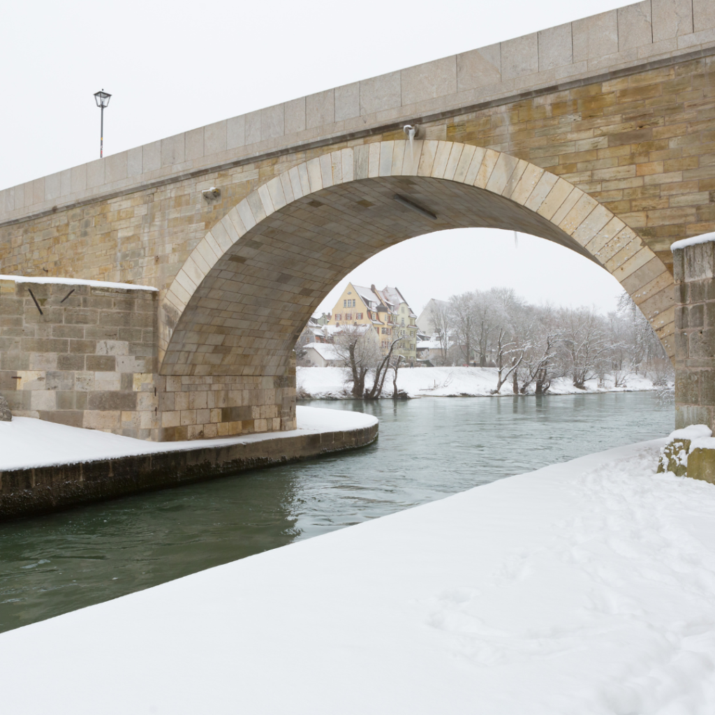 Eine Brücke über einen Fluss. Die Landschaft ist leicht mit Schnee bedeckt.